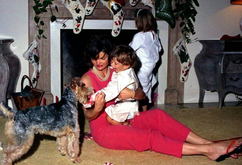 Photographer:    Stoughton, Cecil W. (Cecil William), 1920-2008 Description:First Lady Jacqueline Kennedy sits with her son, John F. Kennedy, Jr. (sitting in the First Ladys lap), on Christmas as John plays with Kennedy family dog, Charlie; Caroline Kennedy stands at right (back to camera). Residence of C. Michael Paul, Palm Beach, Florida. 